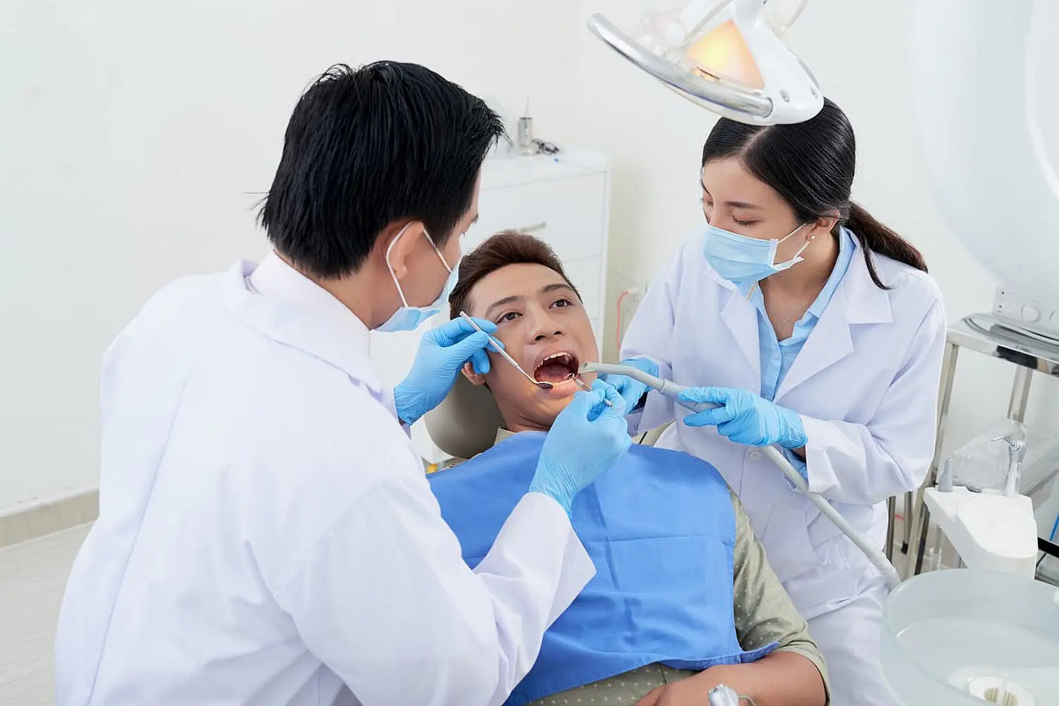 At Happy Smiles Orthodontics in St. Augustine, FL, a dentist and dental assistant wearing masks and gloves perform a dental procedure on a patient with tongue thrust seated in the dental chair.