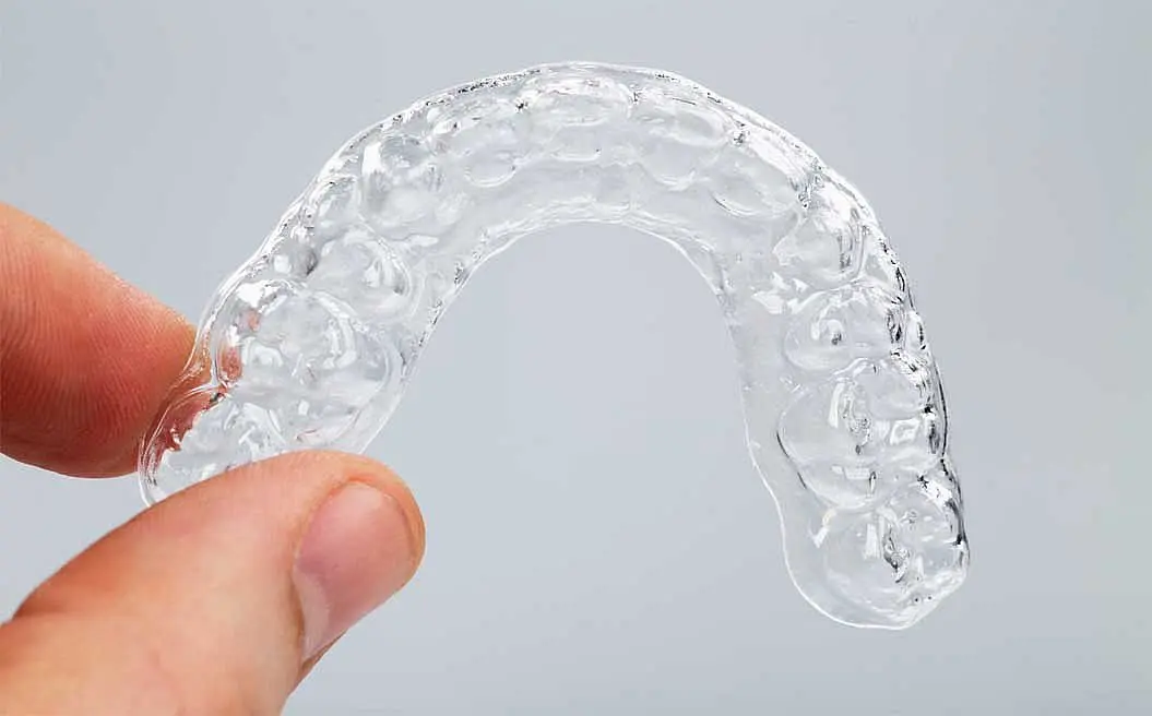 A hand displays a clear Essix Retainer or mouthguard against a plain background at Happy Smiles Orthodontics in St. Augustine, FL.