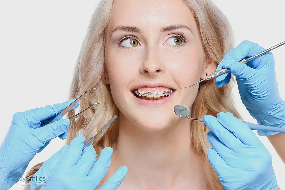 At Happy Smiles Orthodontics, a woman with braces for overbite in St. Augustine, FL is examined using various dental tools held by gloved hands against a white background.