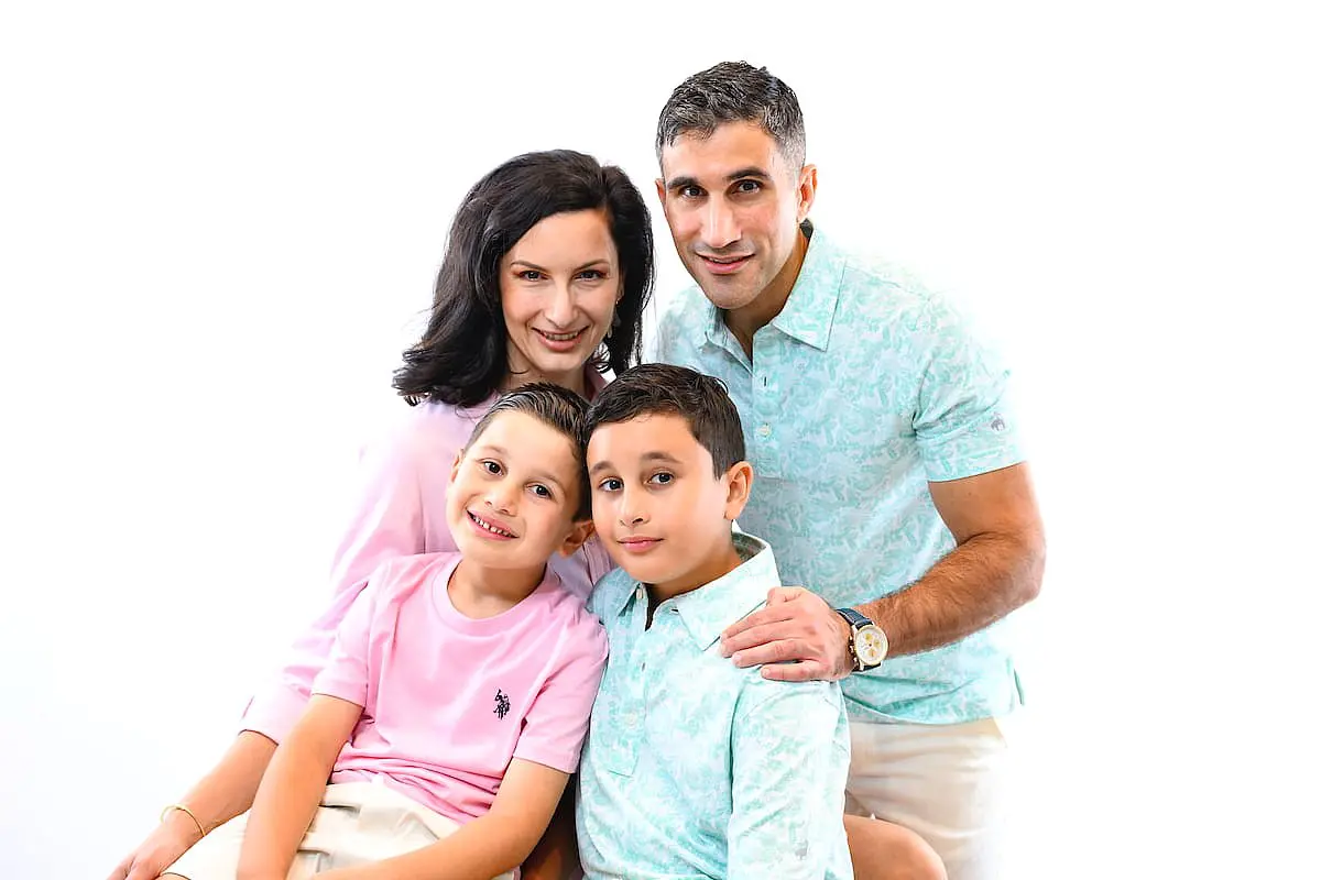 Dr. Mark Komforti's family of four smiles together at Happy Smiles Orthodontics in St. Augustine, FL, adults behind children, white background.