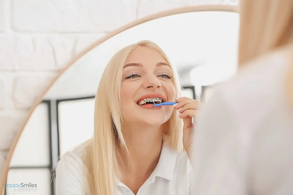 young woman metal braces toothbrush home - How to Floss with Braces in St. Augustine, FL